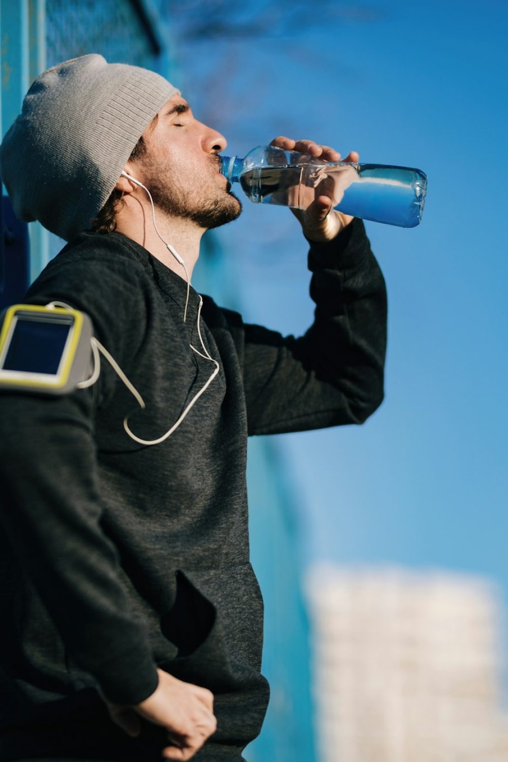 Below view of athletic man drinking water while exercising outdoors.